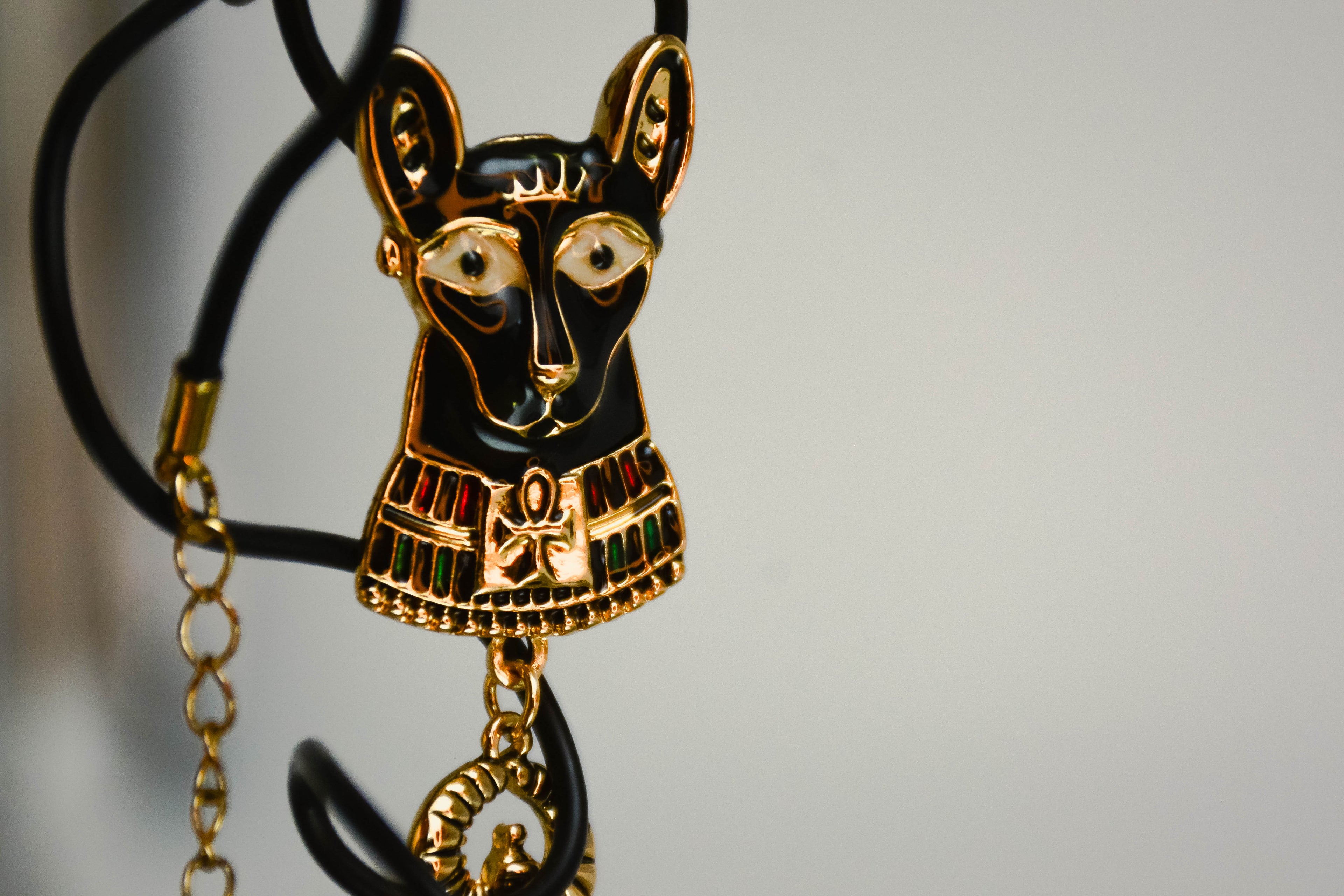 Bastet pendant with gold detailing next to it, on off-white with  soft grey details background. 