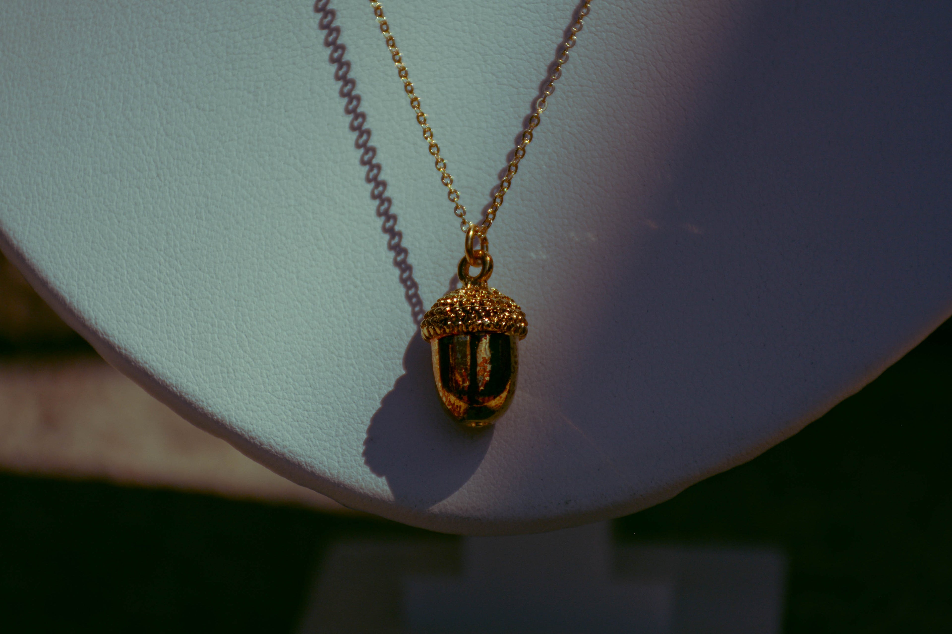 Gold dainty acorn necklace on background with creative lighting. Purple, pink, red, black, and green.