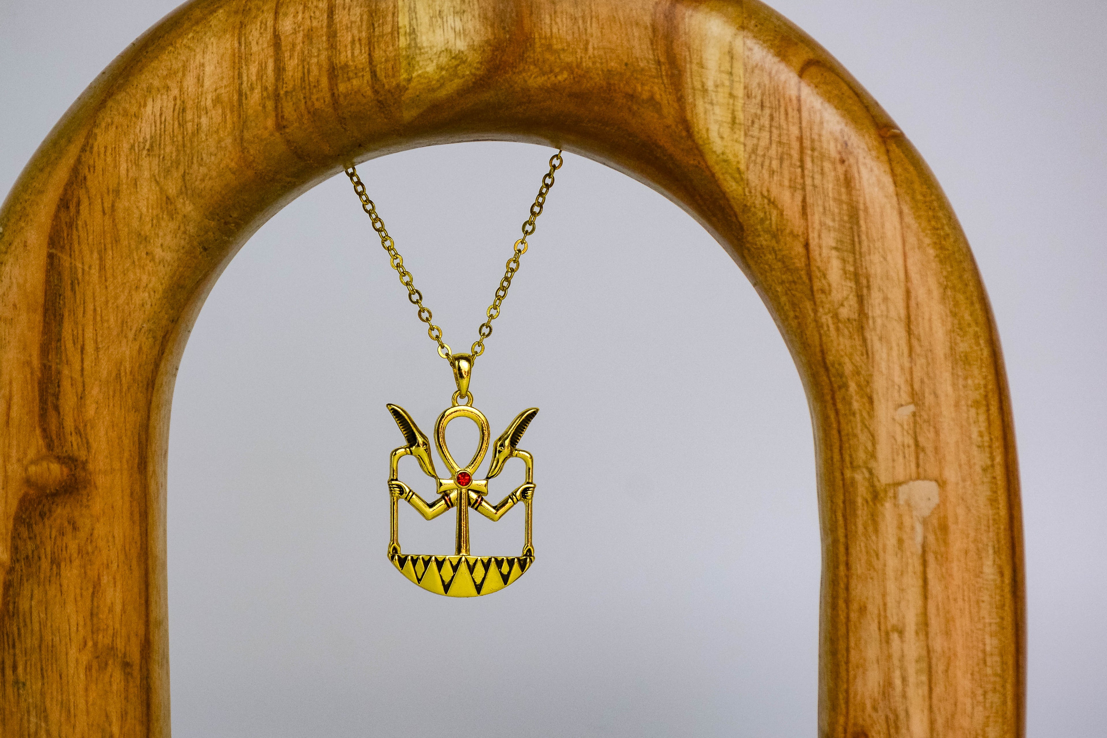 Ankh necklace on wooden arch, off-white background. 