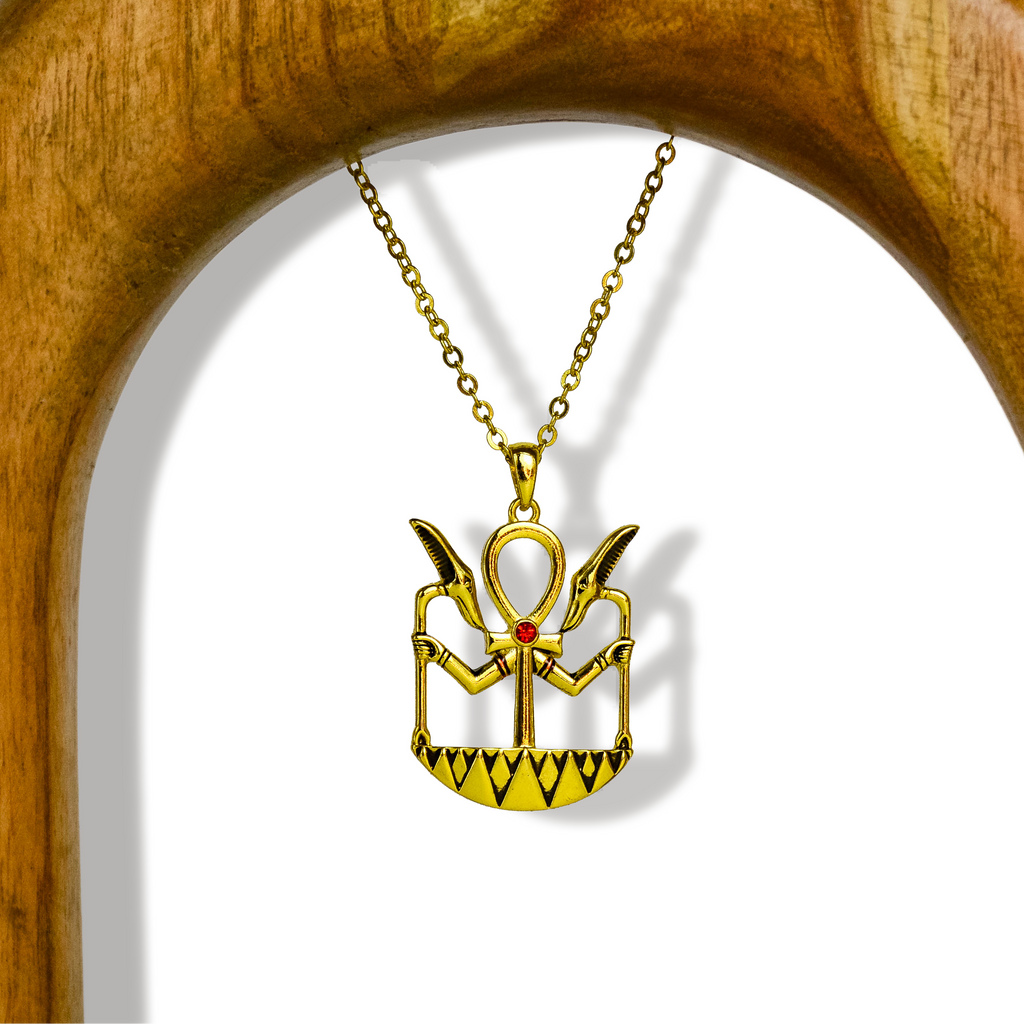 Gold-colored ankh necklace with hangs extending outwards and wings. Black and gold design, as well as square shape around. On gold chain suspended on a wooden arch. White background. 