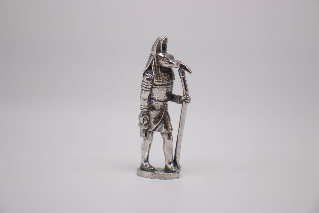 Anubis figurine, silver with black detailing, on off-white background. 