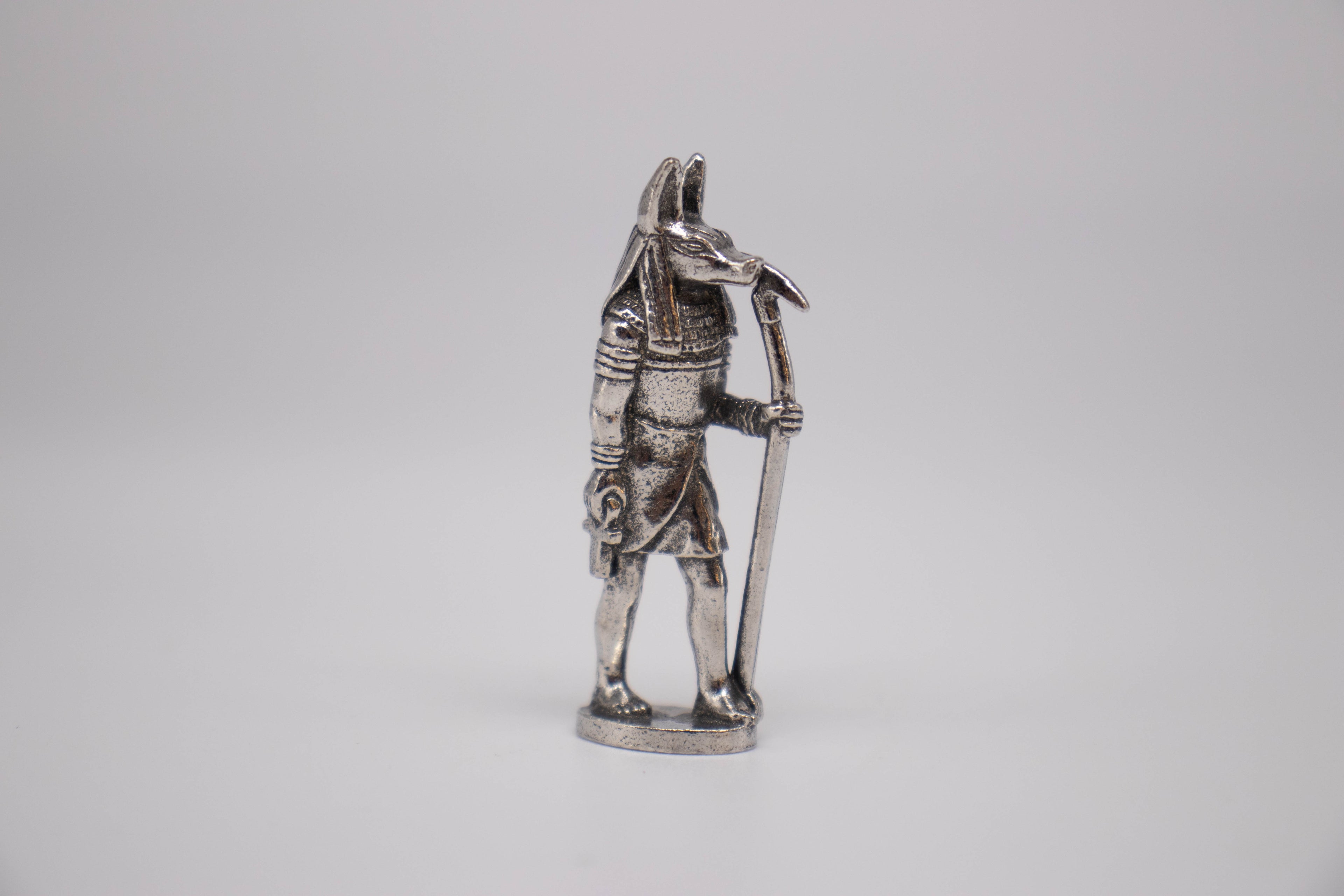 Anubis figurine, silver with black detailing, on off-white background. 