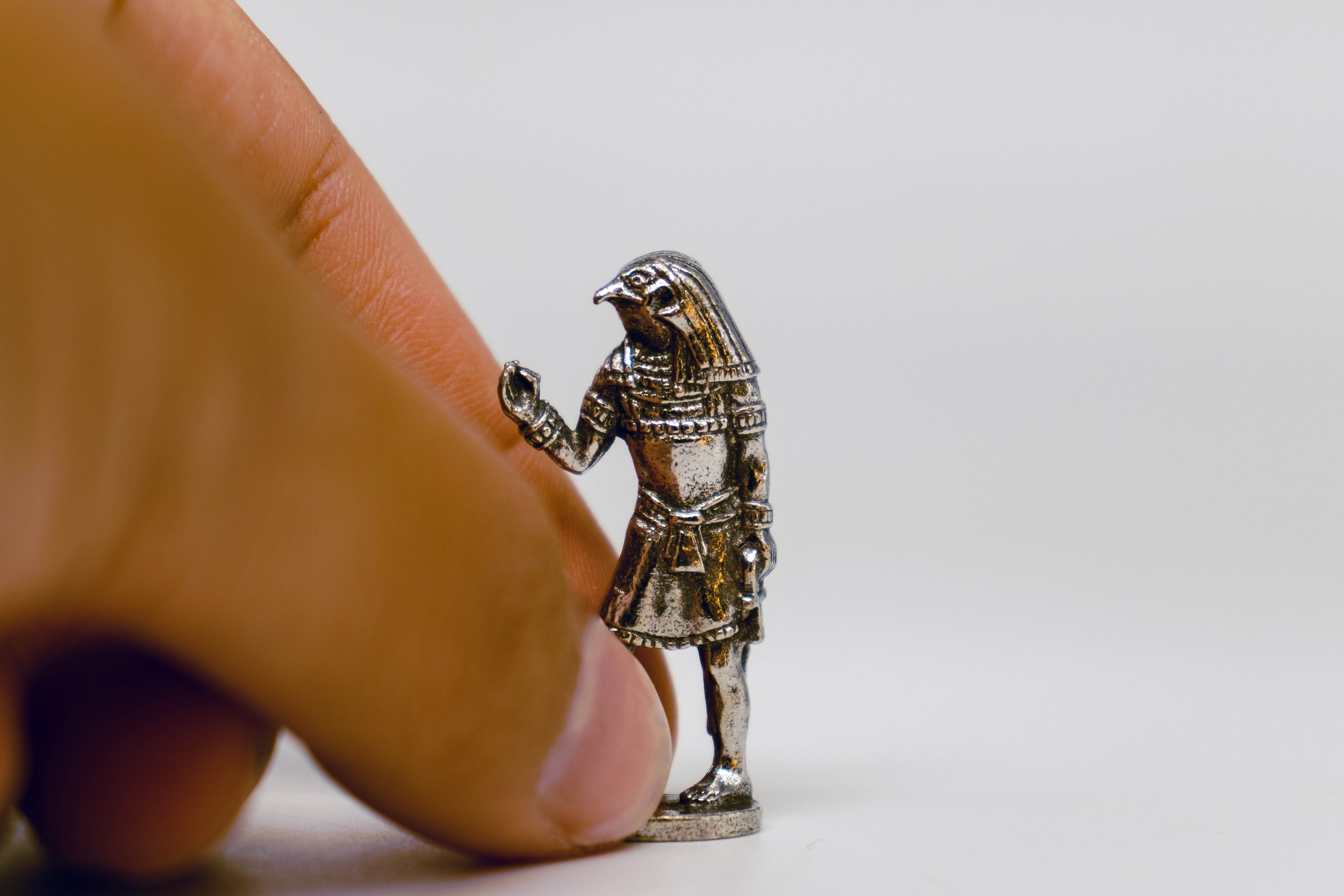 Horus figurine, silver with black detailing, on off-white background. Hand is picking up figuring for size comparison. 