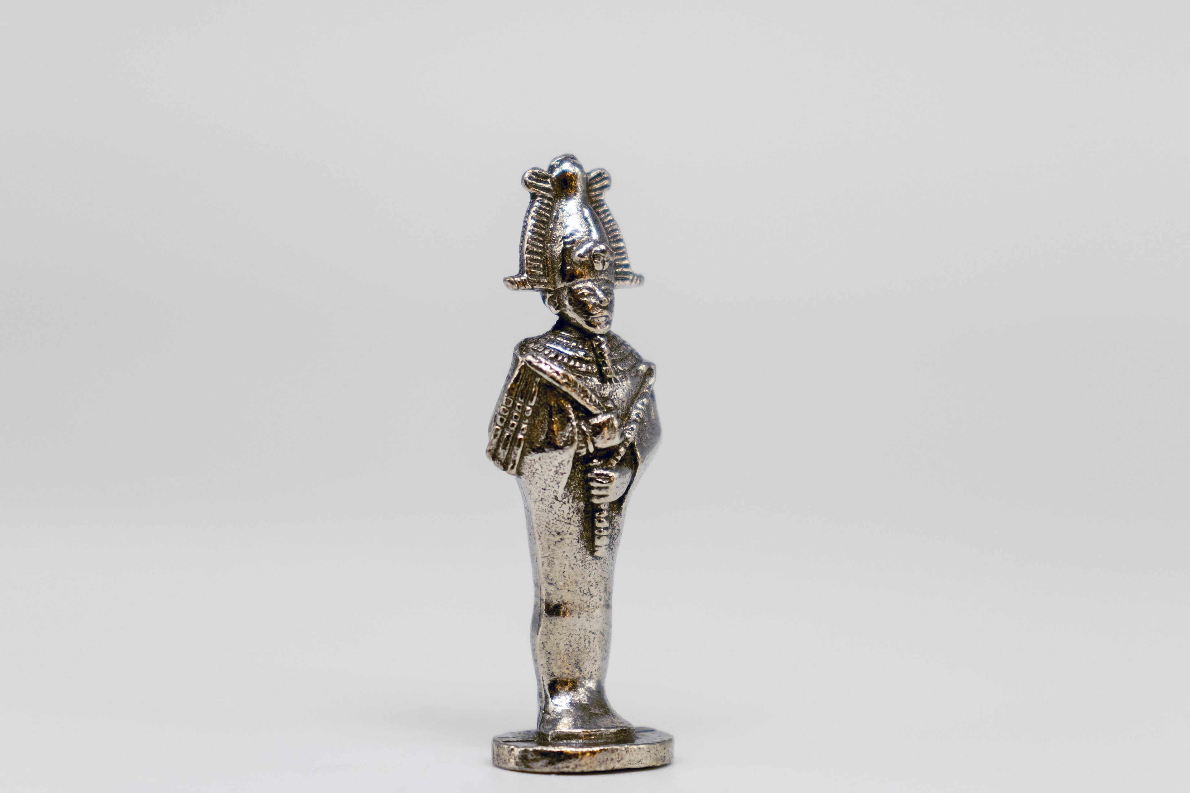 Osiris figurine, metal and silver color with black detailing. Off-white background.