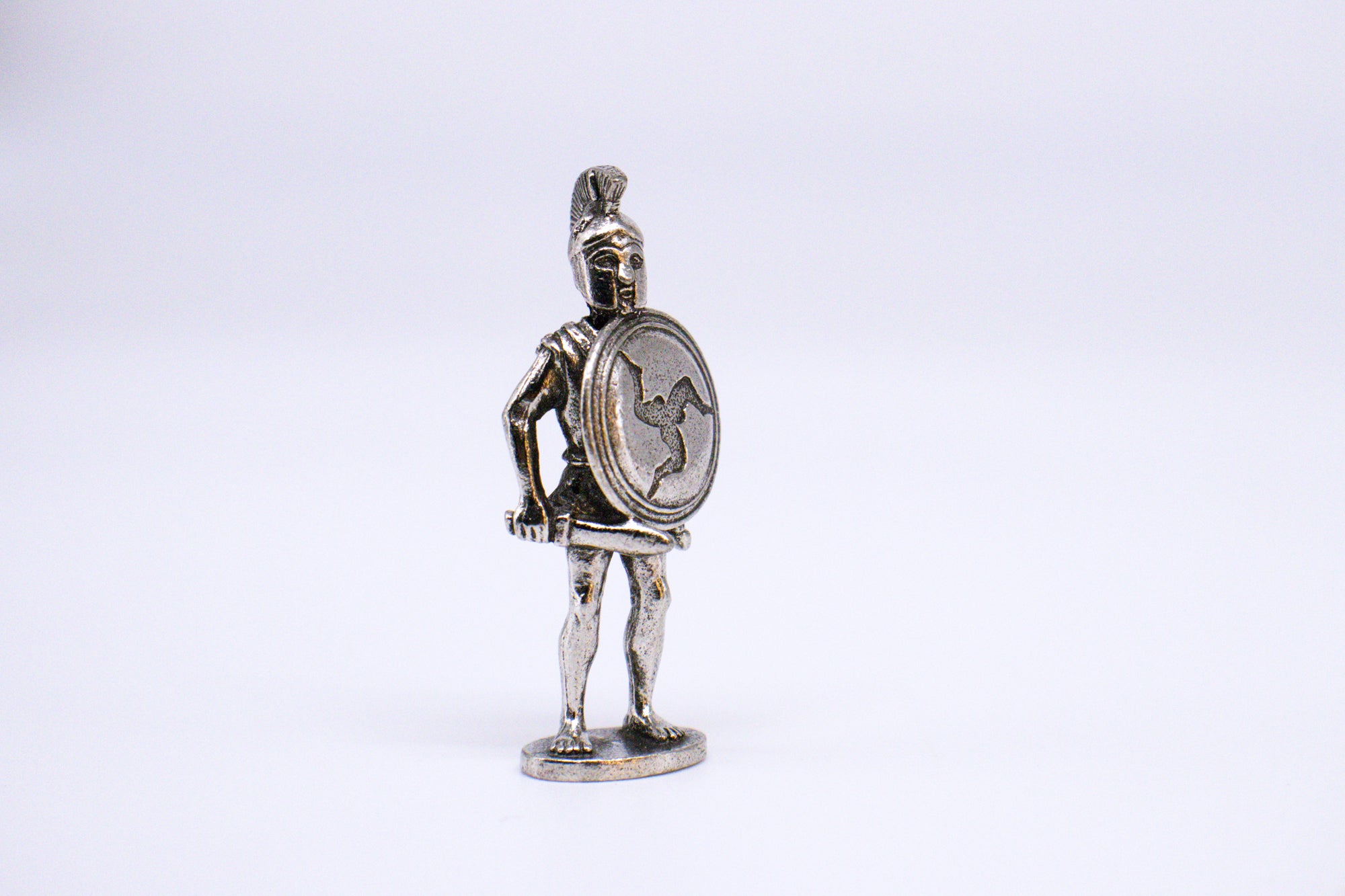 Silver Athenian Hoplite figurine holding sword and shield, on small pedestal. White background. 