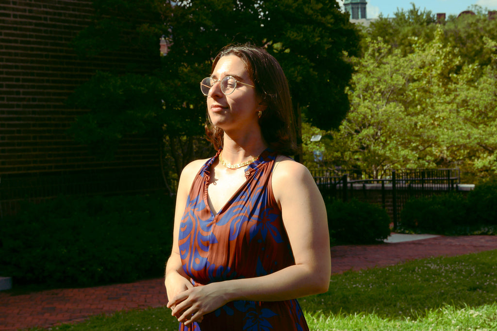 Meander earrings being worn alongside necklace. Model is visible from torso up wearing a terracotta and purple dress. Model is posing elegantly. 