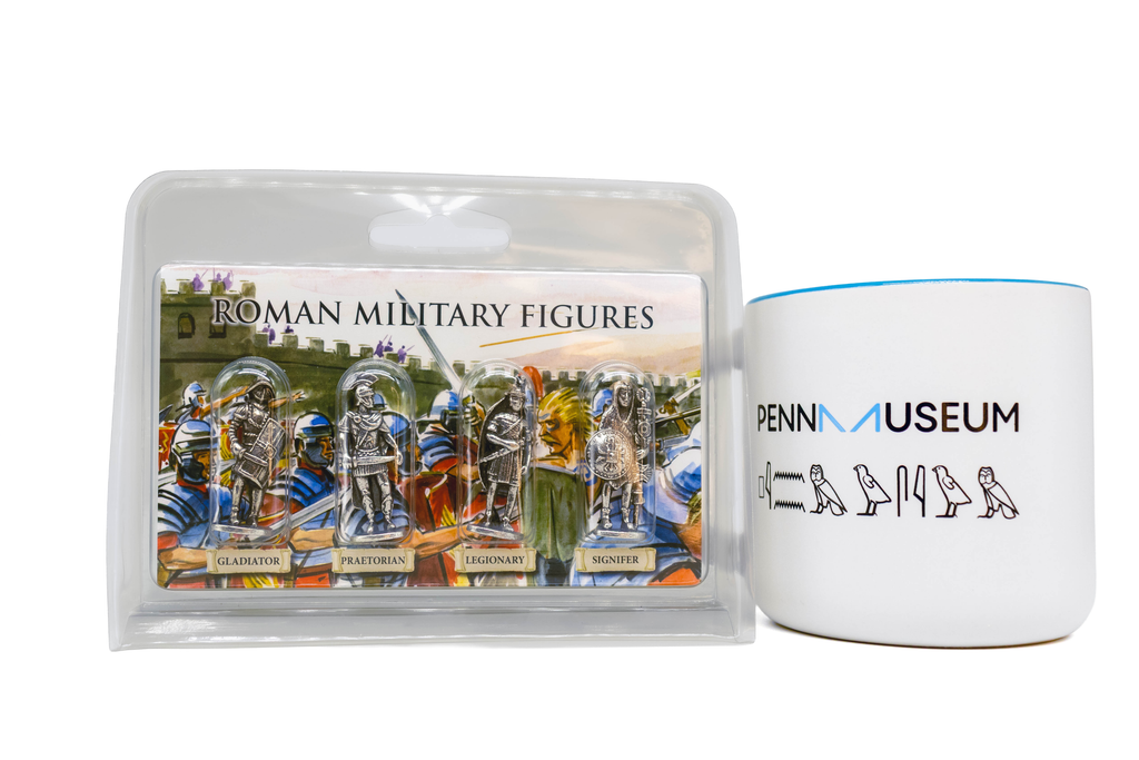 Four Roman military figures in plastic packaging next to Penn Museum mug, white with blue and black details. Mug has museum logo as well as hieroglyphs that spell "Penn Museum". White background. 
