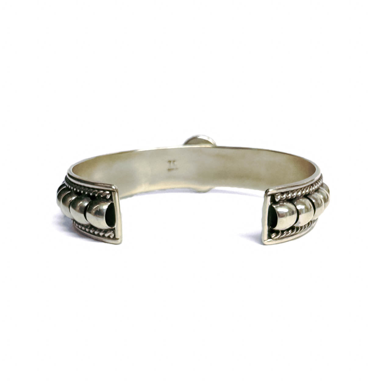 Back (inside) view of a silver bracelet featuring artistic accents and a turquoise stone at the center (facing away and not visible aside for silver setting). Bracelet is on a white background.