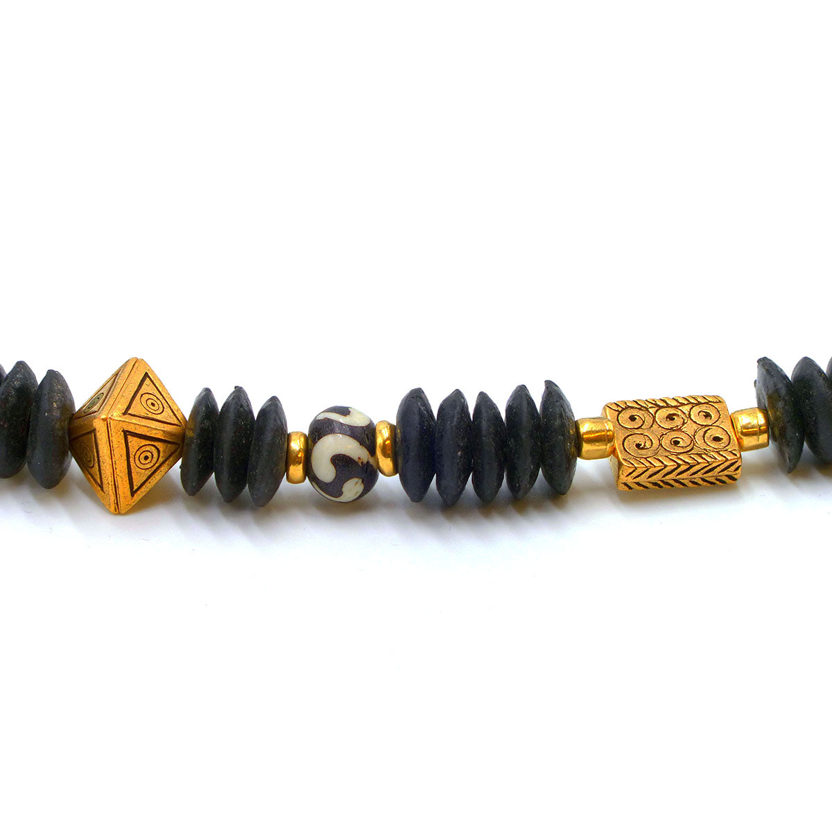 Close up of gold plated and ceramic beads of African design necklace on white background.